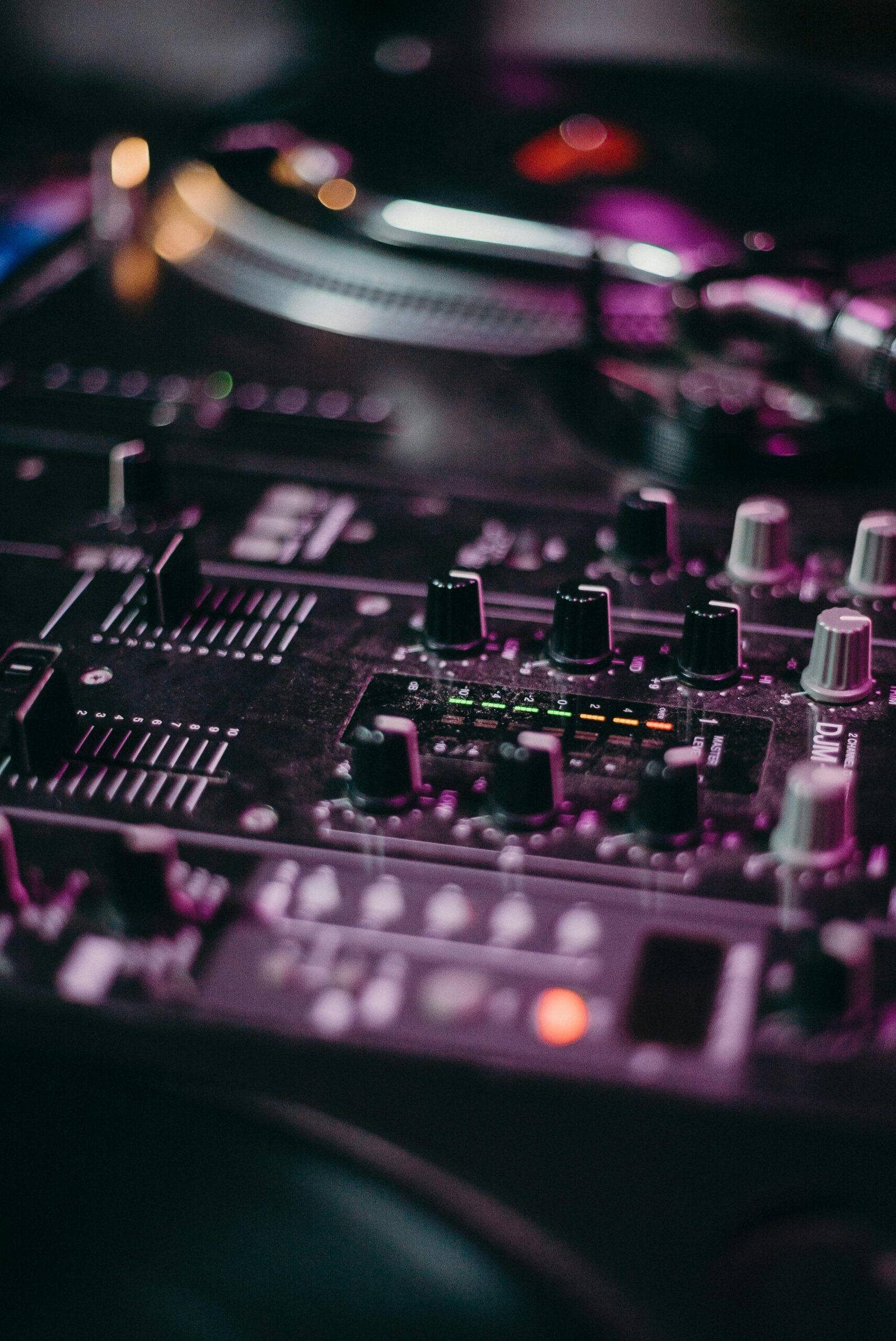 A close-up view of a DJ mixer with illuminated controls in a vibrant setting.